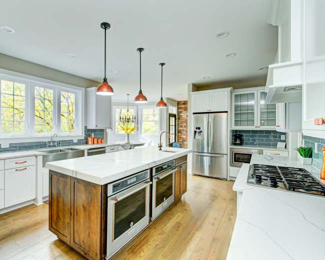 A modern kitchen features white cabinetry, stainless steel appliances, and a large island with a quartz countertop.