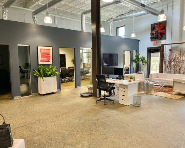 The image shows a modern office space featuring a reception area with a desk, potted plants, and multiple glass-walled meeting rooms.