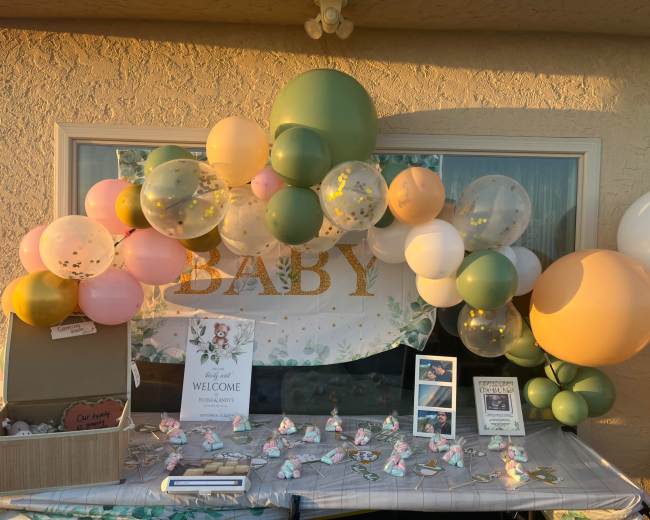 A decorative arch made of colorful balloons frames a welcome sign at a baby shower setup.