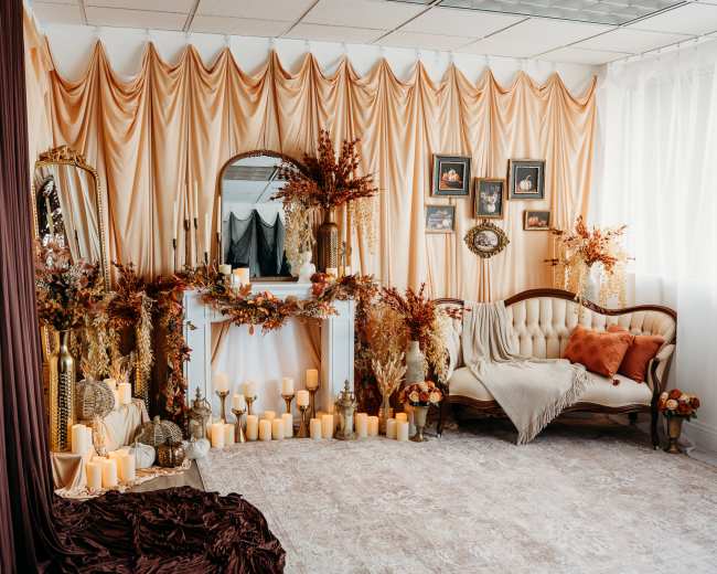 The image shows a decorated room with draped fabric in soft hues, a vintage sofa, a mirror, and various candles arranged among floral decorations.