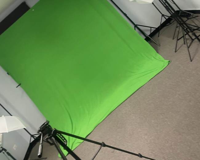 A photography studio with a green backdrop and multiple light umbrellas positioned on stands.