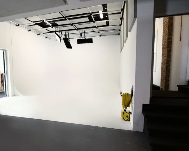 A blank, white studio space with industrial lighting and yellow cables on the floor.