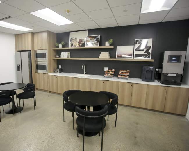 A modern break room with two circular black tables, a countertop with kitchen appliances, and a wall featuring decorative art pieces.
