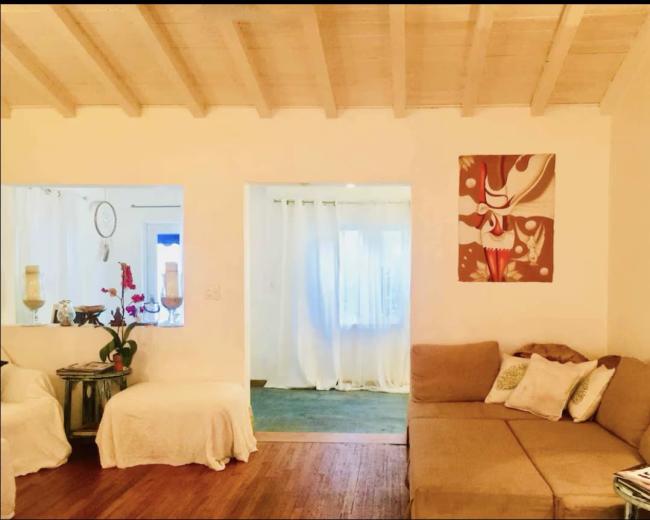 The image shows a living room with a beige sofa, a small table with a plant, and a doorway leading to another bright room.