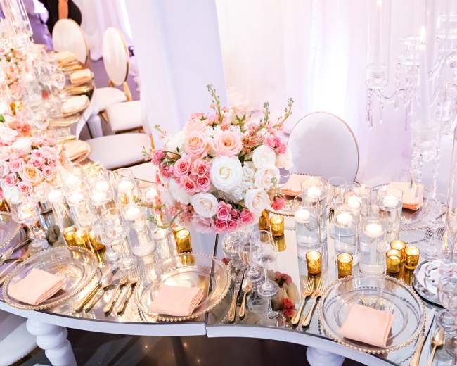 A beautifully arranged dining table features an elaborate floral centerpiece with roses, surrounded by candles and elegant tableware.