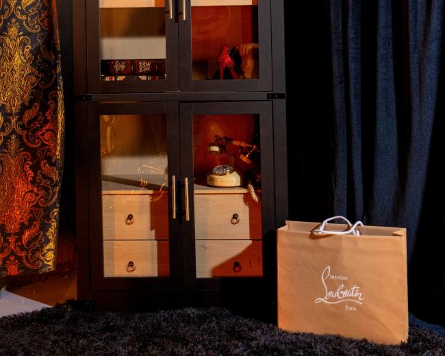 The image features a tall, black display cabinet with glass doors, showcasing decorative items, and accompanied by a shopping bag from a boutique.