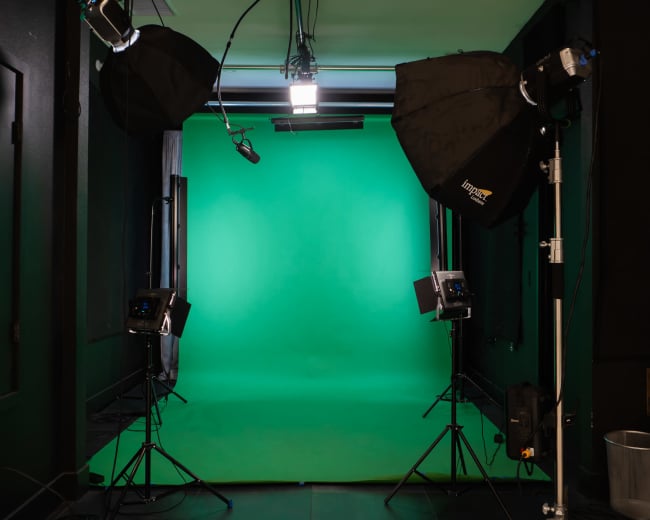 The image shows a photography studio featuring a green screen backdrop, with several studio lights positioned in front of it.