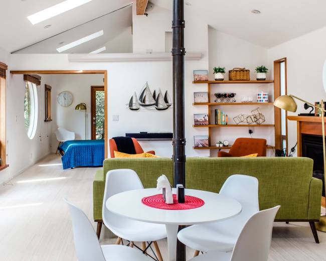 A modern living space features a circular window, a green sofa, a white dining table, and a separate room visible in the background.