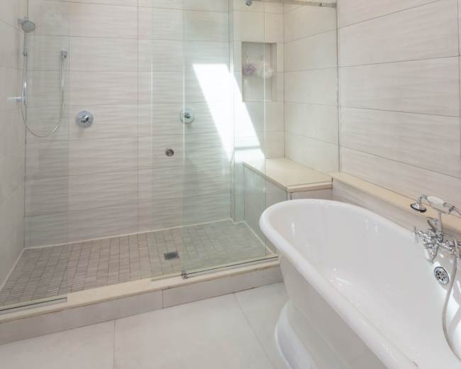A modern bathroom features a glass-enclosed shower and a freestanding bathtub under a skylight.