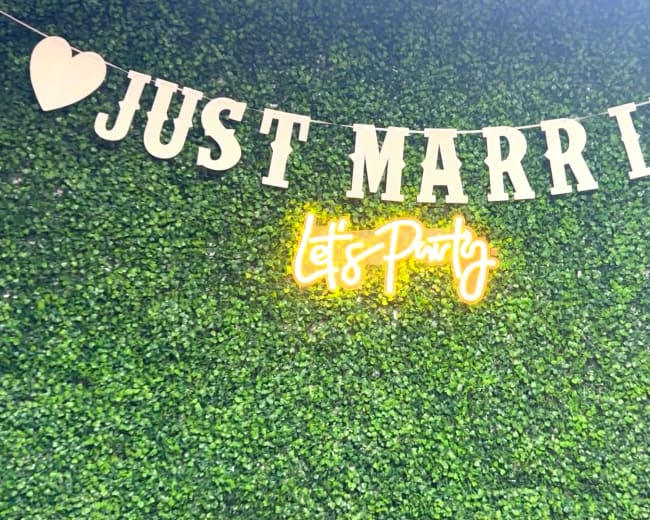 A green backdrop with a banner that reads "Just Married" and a neon sign saying "Let's Party."