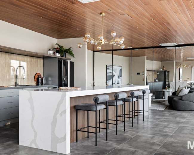 The image shows a modern kitchen with a large island featuring bar stools, sleek cabinetry, and a dining area in an open-concept layout.
