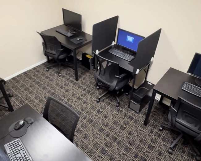 The image shows a small office space with several desks equipped with computer monitors and chairs.