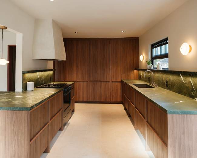 The image shows a modern kitchen with wooden cabinets, green stone countertops, a range hood, and minimal lighting fixtures.