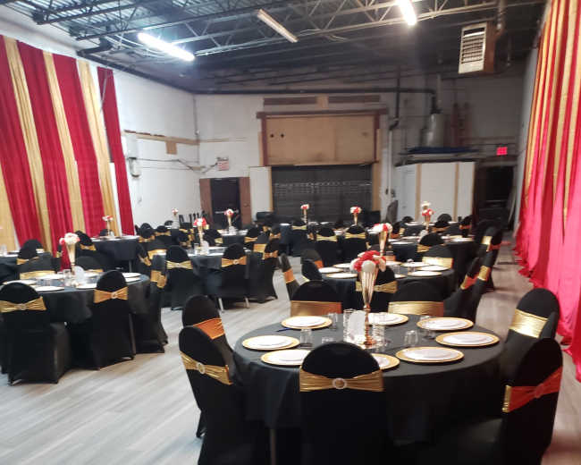 The image shows a banquet hall arranged with round tables covered in black tablecloths and gold-accented chairs, set for dining with plates and centerpieces.