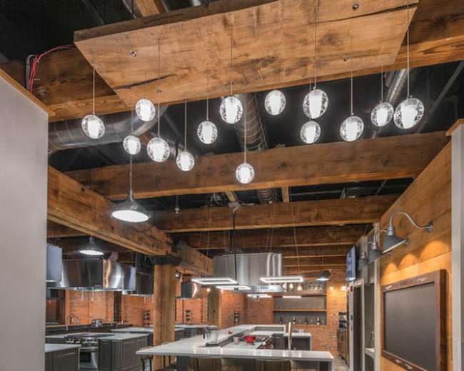 The image shows a modern kitchen with exposed wooden beams, large island seating, and multiple pendant lights hanging from the ceiling.