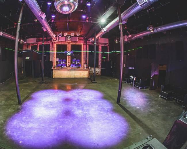 The image shows an empty nightclub with a bar area, a disco ball hanging from the ceiling, and colorful lighting along the walls.