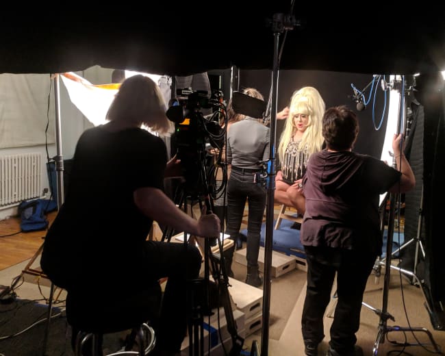 A film crew sets up equipment around a person in costume in a studio setting.