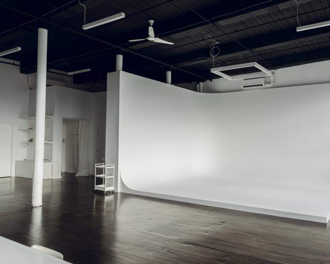 The image shows a spacious studio with a smooth, curved white backdrop and wooden flooring.