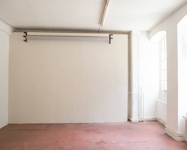 The image shows an empty room with white walls, large windows, and a roll-down screen mounted near the ceiling.