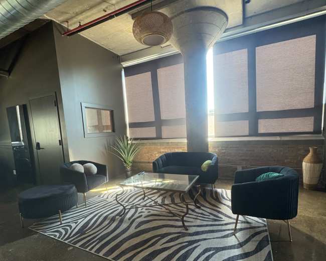 The image shows a modern seating area with two chairs and a sofa arranged around a glass coffee table on a zebra-striped rug under large windows.