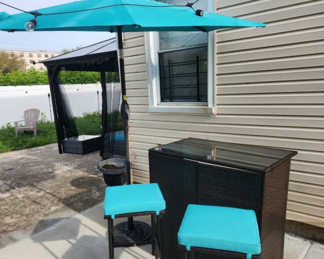 A small outdoor seating area with two turquoise bar stools and a matching umbrella next to a dark wicker bar counter.