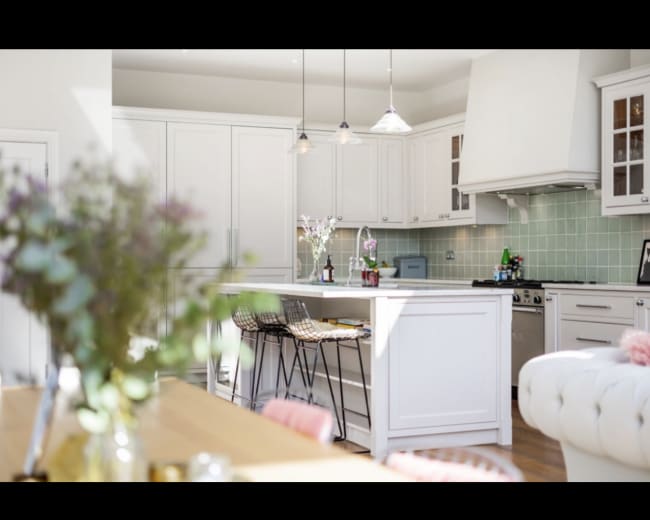 The image shows a modern kitchen with white cabinetry, a large island, and pendant lighting above the counter.
