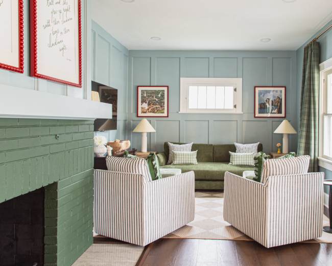 The image shows a cozy living room featuring a green sofa against a blue paneled wall, flanked by two striped armchairs and a small side table.
