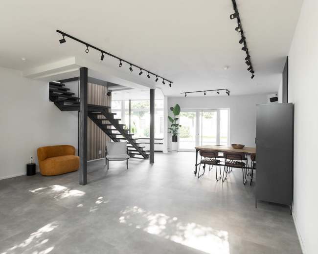The image shows a modern, open-concept living space with a staircase, large windows, and a dining area.