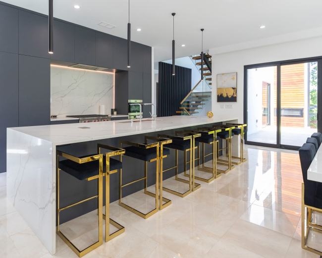 The image showcases a modern kitchen with a large marble island, black cabinetry, and gold-accented bar stools.