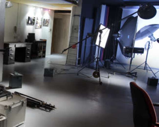 The image shows a modern kitchen space connected to a professional photography studio, featuring various lighting equipment and a workstation.