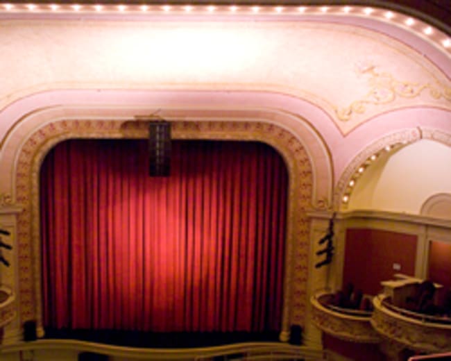 The interior of a theater with a red curtain and ornate architecture.