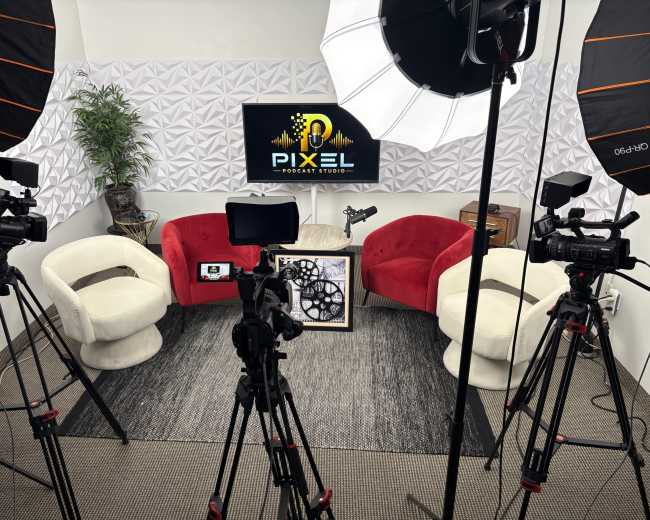The image shows a podcast studio with two red and white chairs, several cameras on tripods, a light setup, and a television displaying the Pixel Podcast Studio logo in front of a textured wall.