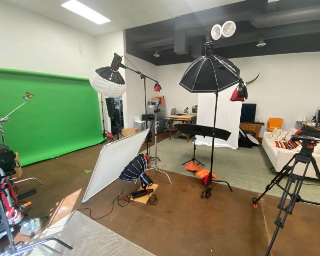 A photography studio equipped with various lights, a green backdrop, and a comfortable seating area.