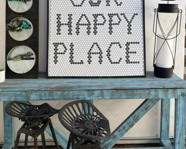 A large sign reading "THIS IS OUR HAPPY PLACE" is displayed on a wall above a blue wooden table and two black stools.