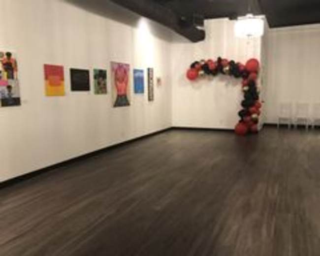 The image shows a spacious indoor venue with artwork displayed on one wall and a decorative balloon arch to the right.