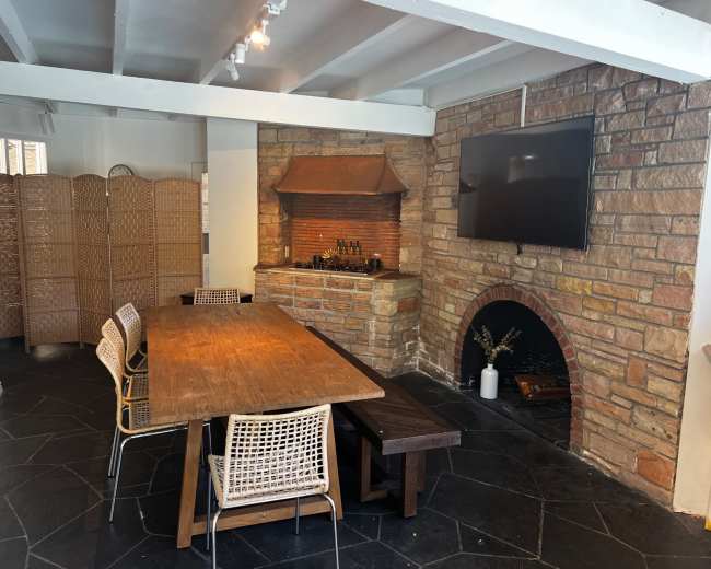 A spacious dining area features a wooden table surrounded by chairs, with a stone fireplace and a television mounted on the wall.