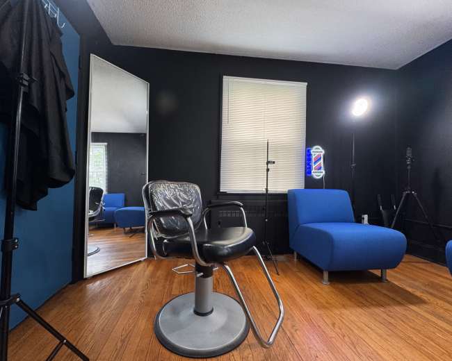 The image shows a barber shop interior featuring a black and blue color scheme, a barber chair, a large mirror, and blue lounge chairs.