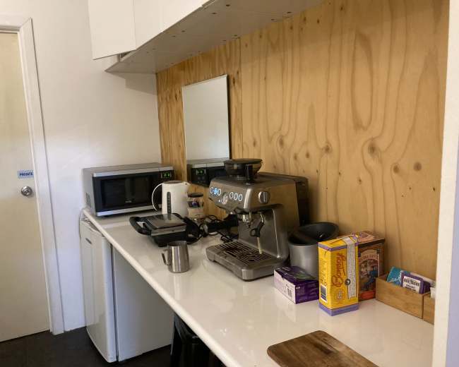 A compact kitchen area features a coffee machine, microwave, and various kitchen items arranged on a countertop against a wooden backdrop.