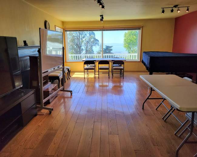 A spacious room features a television, a whiteboard on wheels, chairs arranged for seating, and large windows overlooking a scenic view.