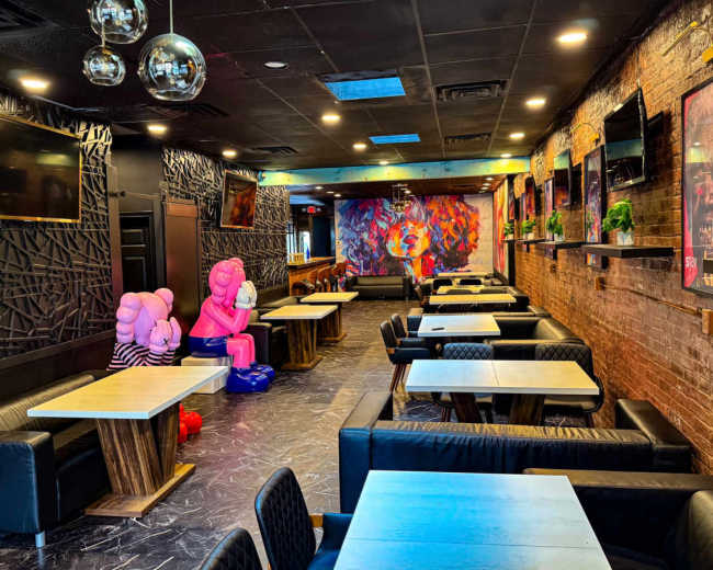 The image shows a stylish restaurant with dark walls, modern furniture, and colorful artwork adorning one wall, along with large seating areas and playful decorations.