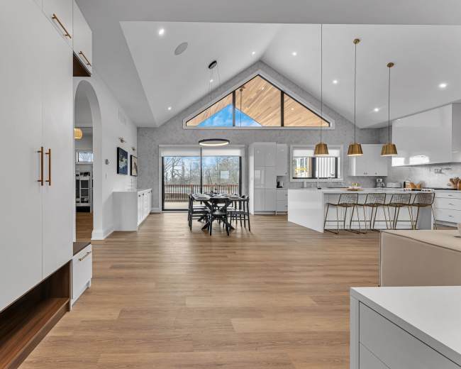 A modern kitchen and dining area with large windows, wooden flooring, and high ceilings featuring a triangular design.