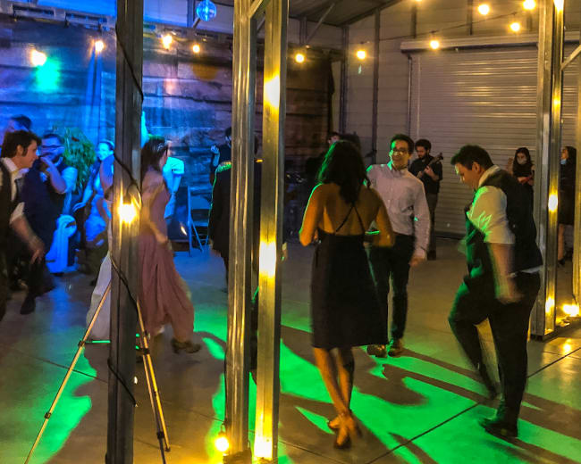A group of people dances under string lights in a large indoor space with colorful lighting.
