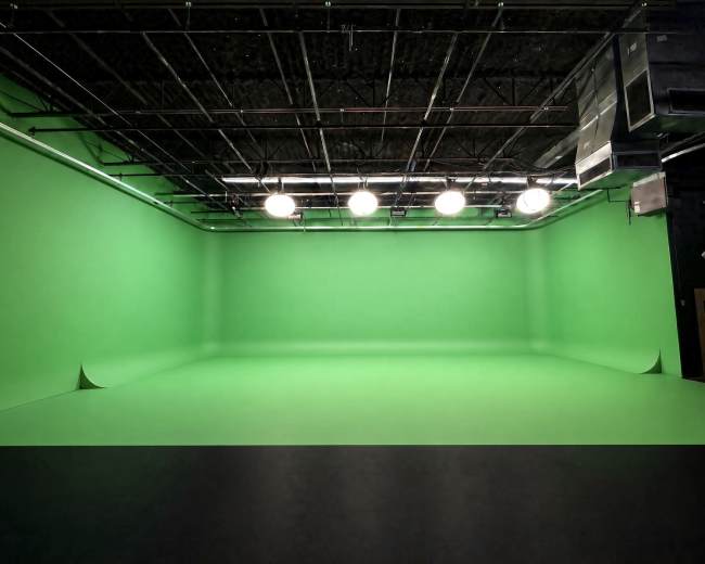 The image shows a large green screen studio with bright overhead lights and a seamless green backdrop.