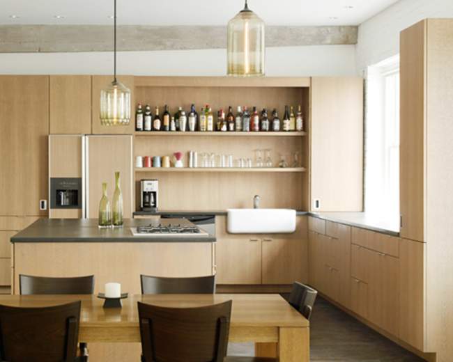 A modern kitchen features wooden cabinetry, a central island with a stovetop, and a dining table set with candles.