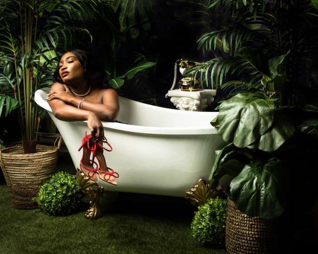 A woman reclines in a white bathtub surrounded by lush greenery and decorative plants.