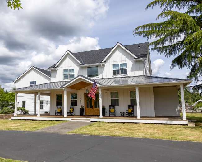A large, modern two-story white house with a covered front porch and an American flag displayed.