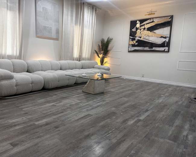 The image shows a modern living room with a plush white sectional sofa, a glass coffee table, and light-colored walls adorned with artwork and curtains.