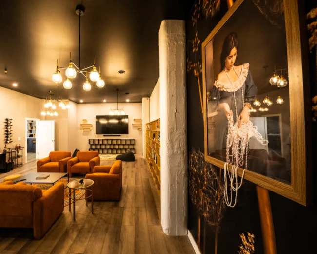 A modern lounge area with orange sofas, decorative lighting, and a large wall mural of a woman wearing pearls.