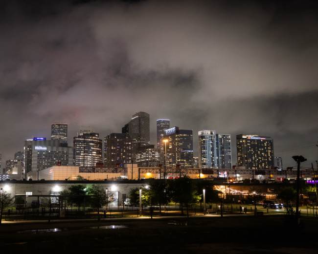 A skyline of Houston, Texas, is illuminated by city lights under a cloudy night sky.