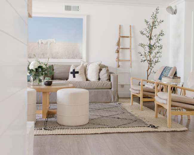 A light and airy living room with a beige couch, wooden furniture, and a decorative ladder against the wall.